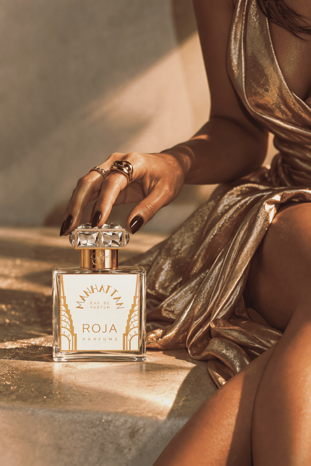 Предметный визуал: флакон Roja Parfums Manhattan, рука с кольцами на крышке, золотая ткань